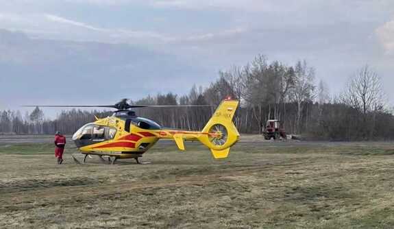 śmigłowiec LPR na polu w tle drzewa i ciągnik roliczy