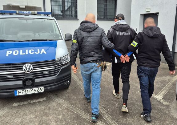 nieumundurowani policjanci prowadzą zatrzymanego mężczyznę w kajdankach