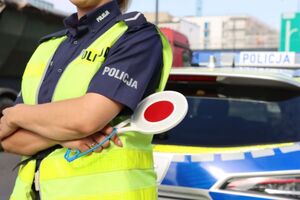 sylwetka policjantki trzymającej tarczę do zatrzymywania kierujących pojazdami, w tle radiowóz