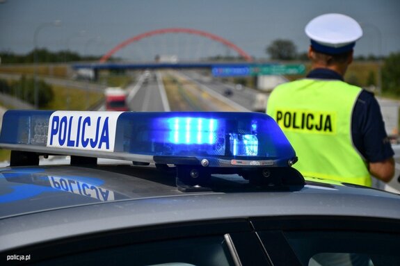 radiowóz i policjant ruchu drogowego, w tle droga z wiaduktem