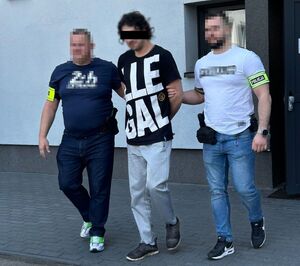 nieumundurowani policjanci prowadzą podejrzanego, w tle budynek