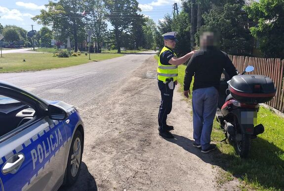 policjant Wydziału Ruchu Drogowego podczas kontroli motorowerzysty, obok radiowóz