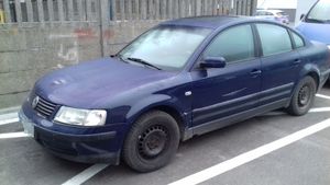 granatowy volkswagen Passat stojący przy betonowym ogrodzeniu, w tle radiowóz.